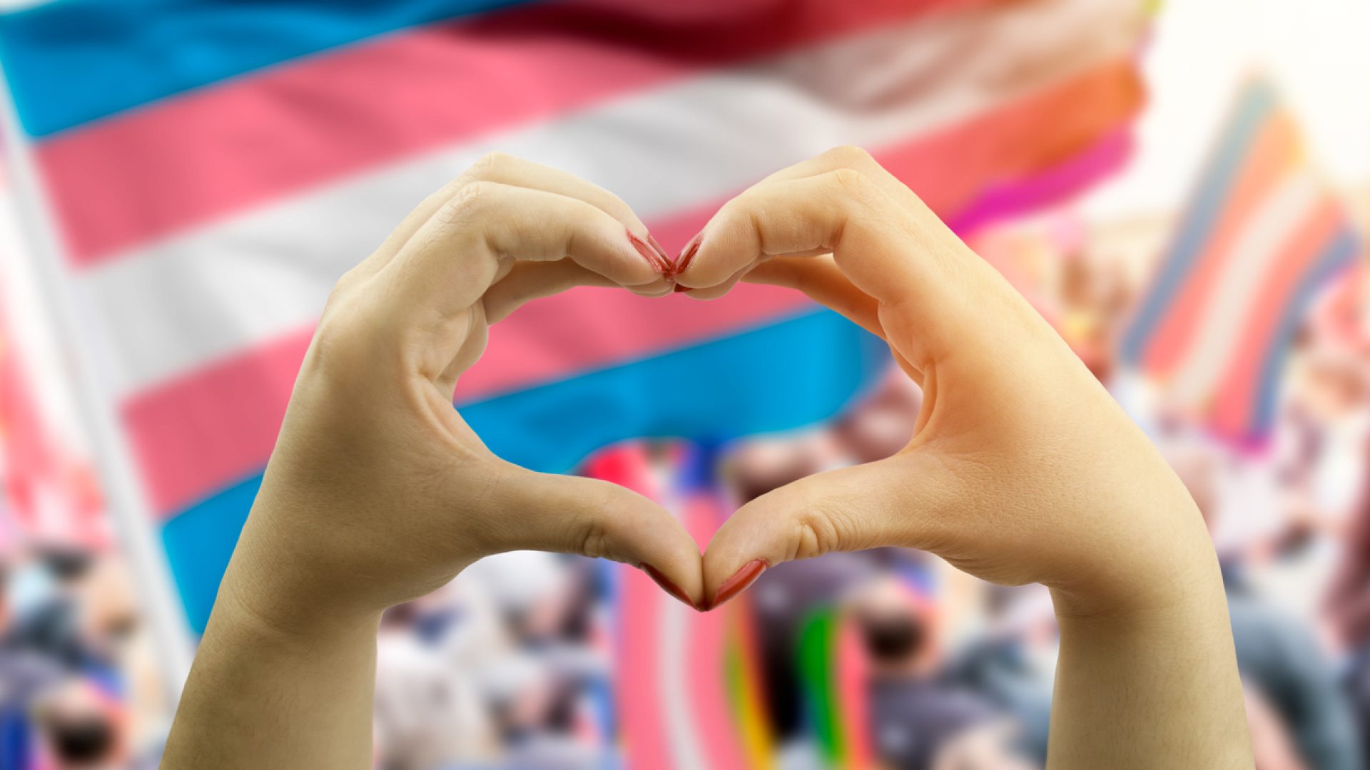 close up hands creating a heart with transgender flag in the background